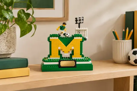 Maquette de football en briques avec base en M, numéro 10 et minifigurine de joueur, exposée sur une étagère.