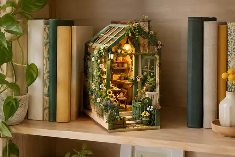 Book nook miniature vert représentant une serre fleurie illuminée, posé entre des livres sur une étagère